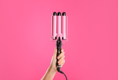 Photo of Woman holding triple curling hair iron on pink background, closeup