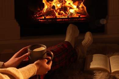 Photo of Woman with cup of drink near fireplace at home, closeup