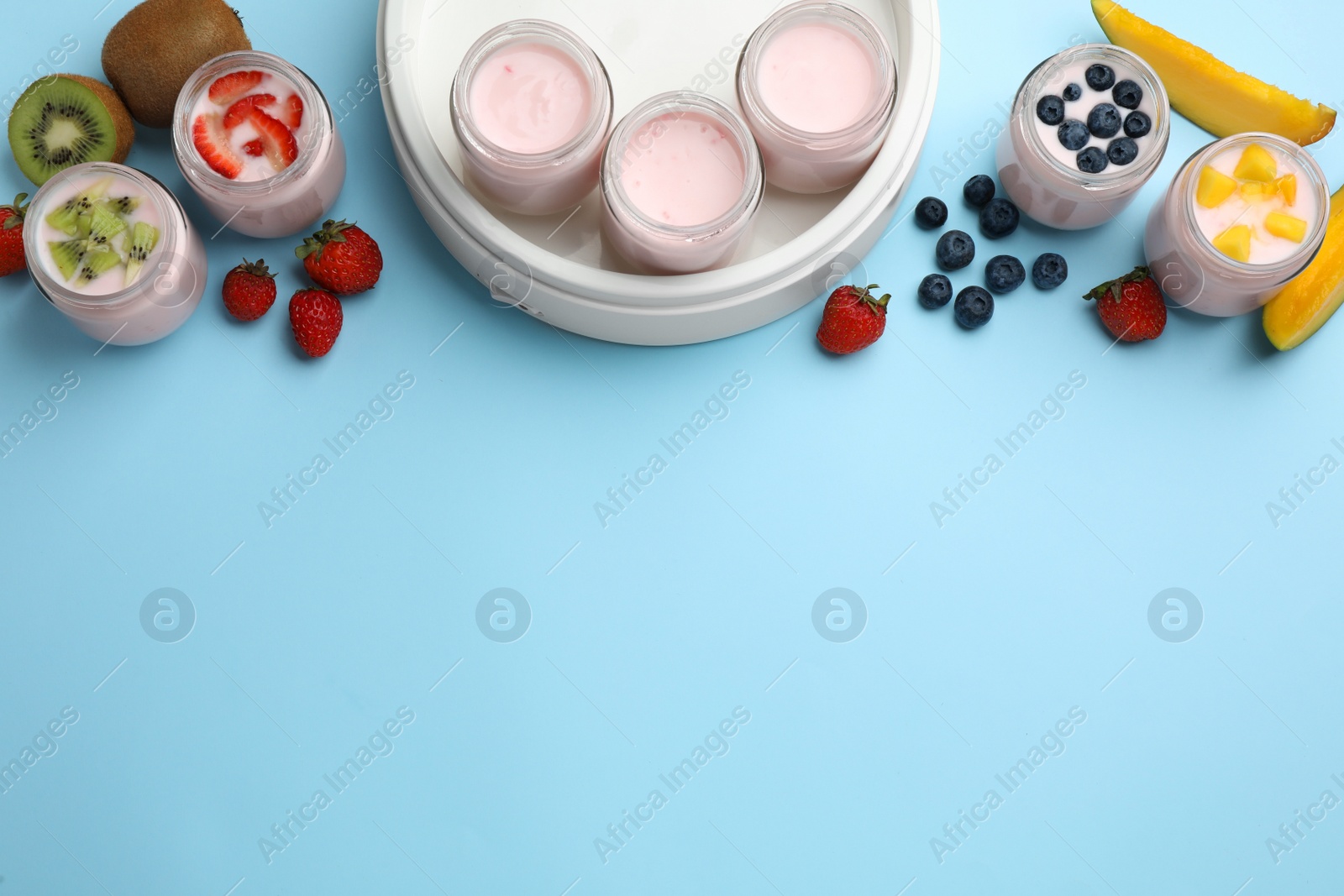 Photo of Tasty yogurt in glass jars and ingredients on light blue background, flat lay. Space for text