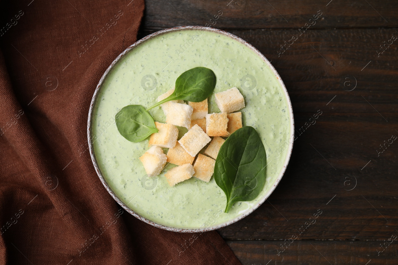 Photo of Delicious spinach cream soup with leaves and croutons in bowl on wooden table, top view