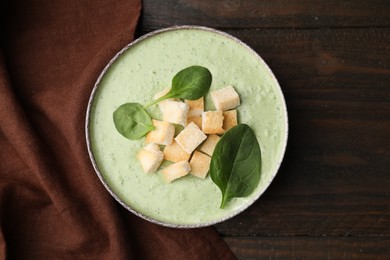 Delicious spinach cream soup with leaves and croutons in bowl on wooden table, top view