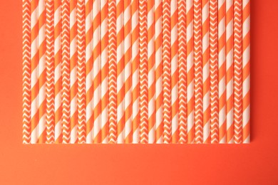 Photo of Many striped paper drinking straws on orange background, flat lay