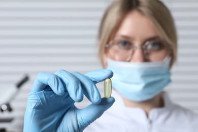 Photo of Doctor holding pill on light background, selective focus