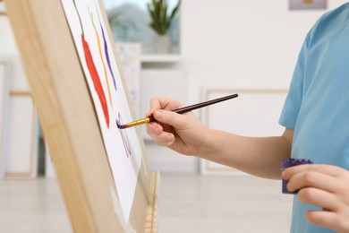 Photo of Little boy painting in studio, closeup. Using easel to hold canvas