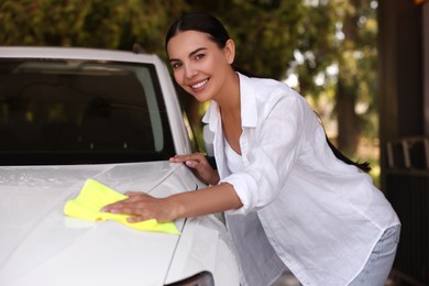 Photo of Happy woman cleaning car hood with rag outdoors