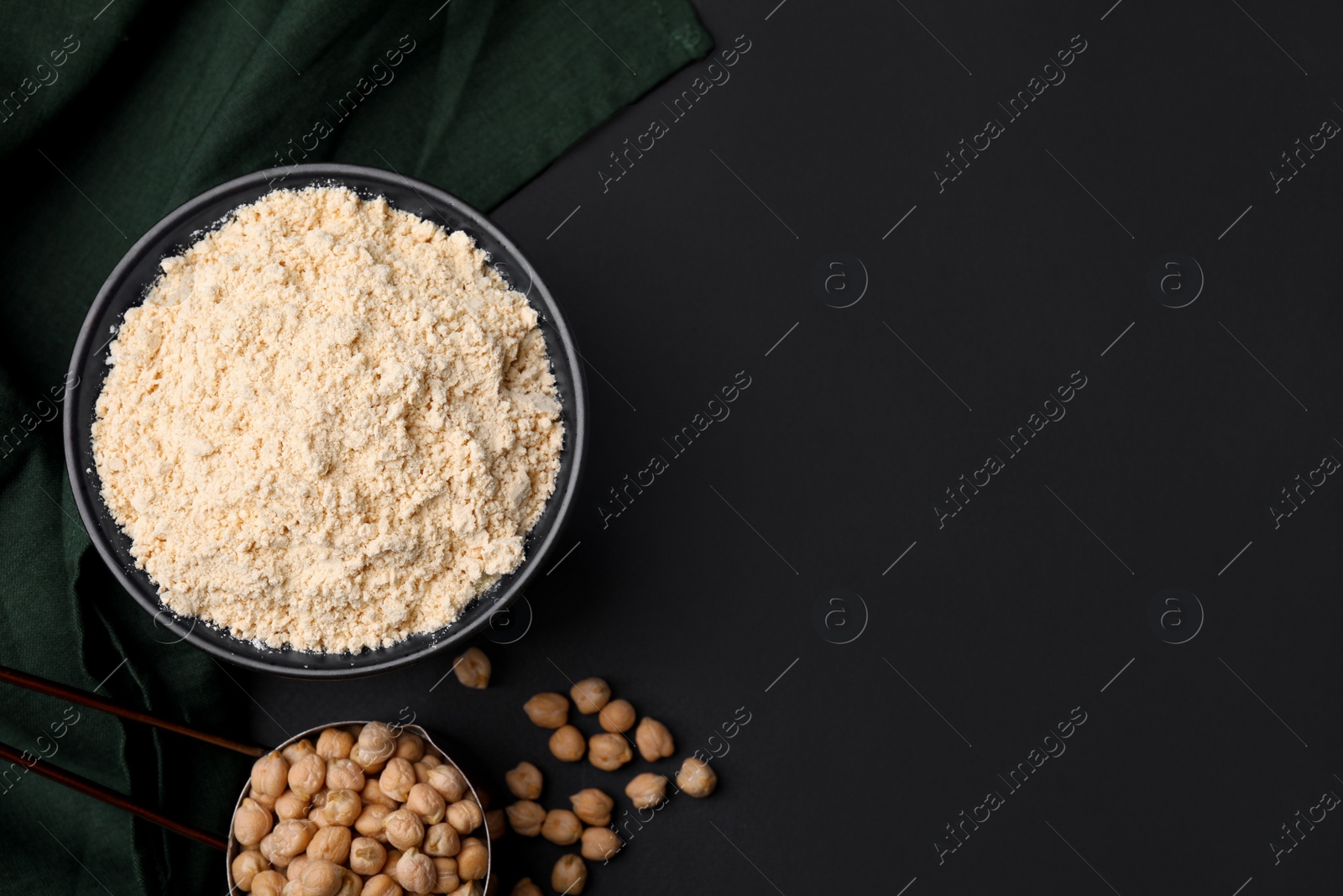 Photo of Chickpea flour in bowl and seeds on black table, flat lay. Space for text