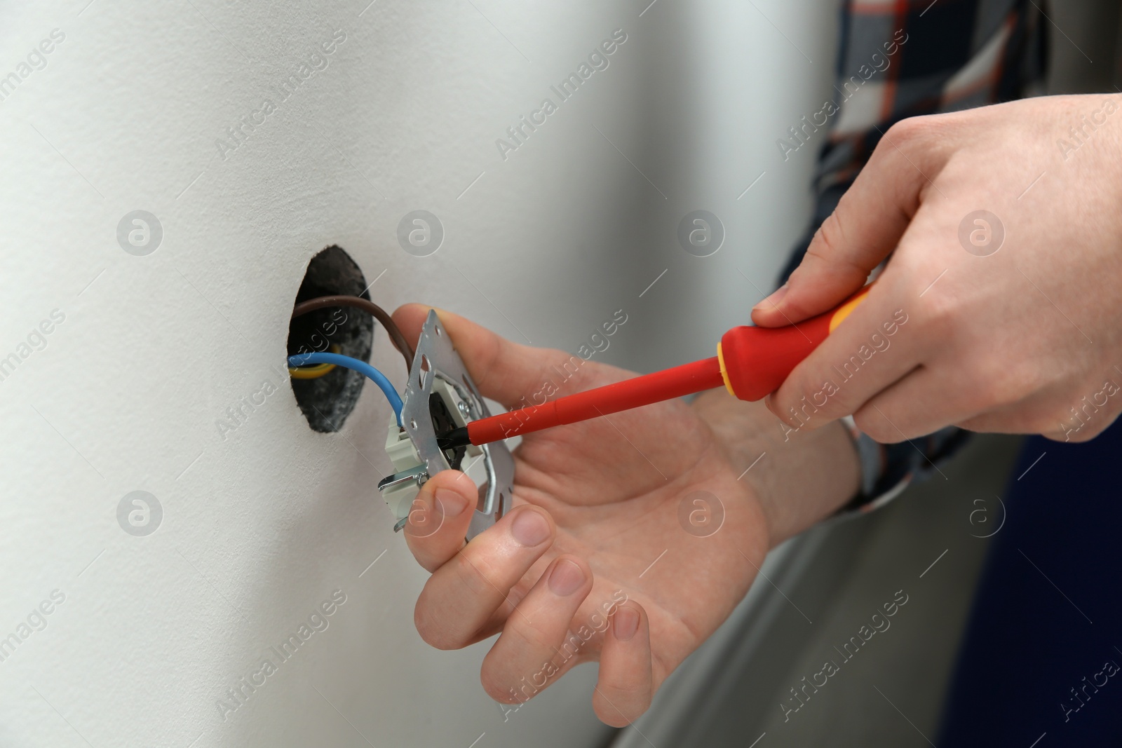 Photo of Electrician with screwdriver repairing power socket indoors, closeup