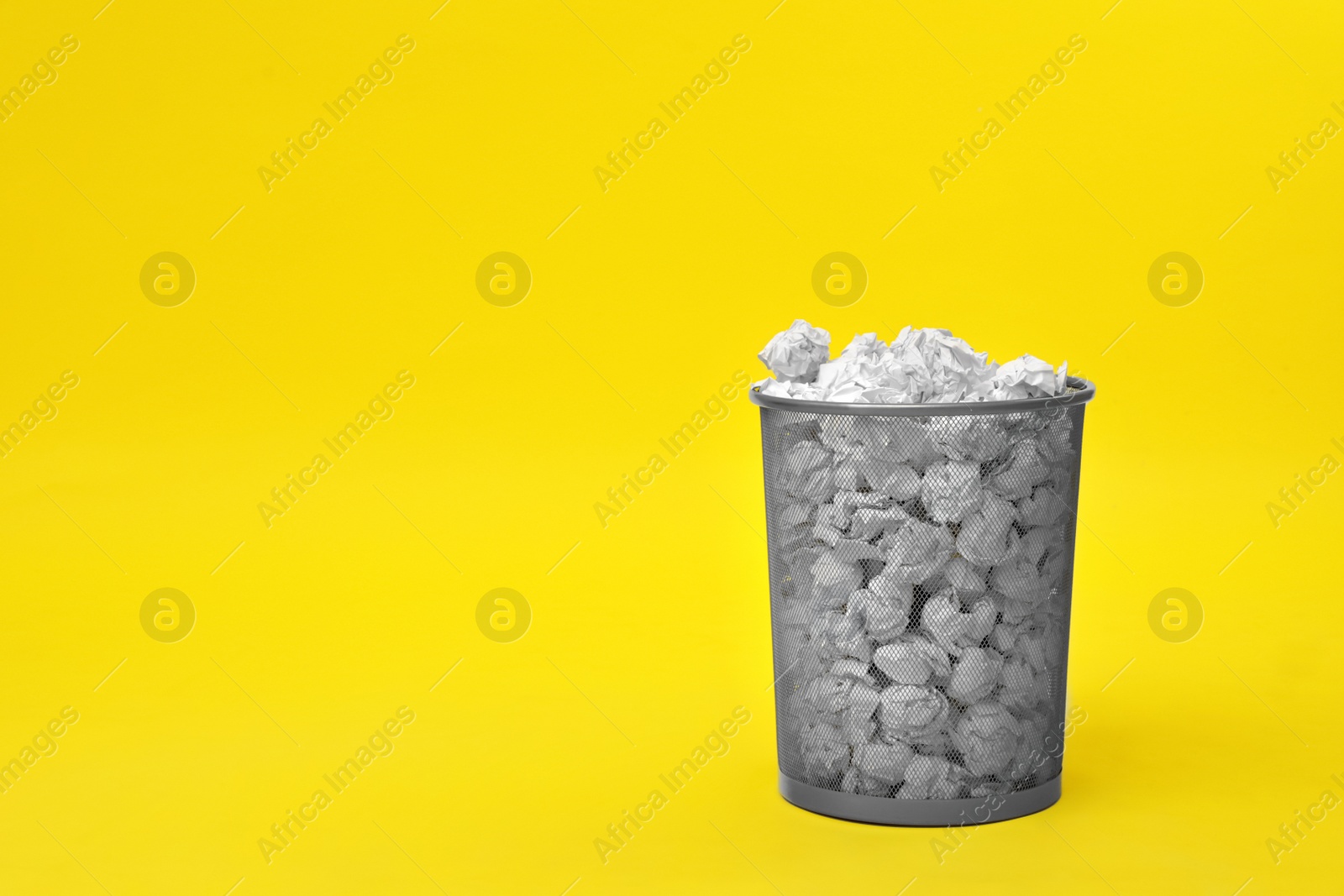 Photo of Metal bin with crumpled paper on color background, space for text