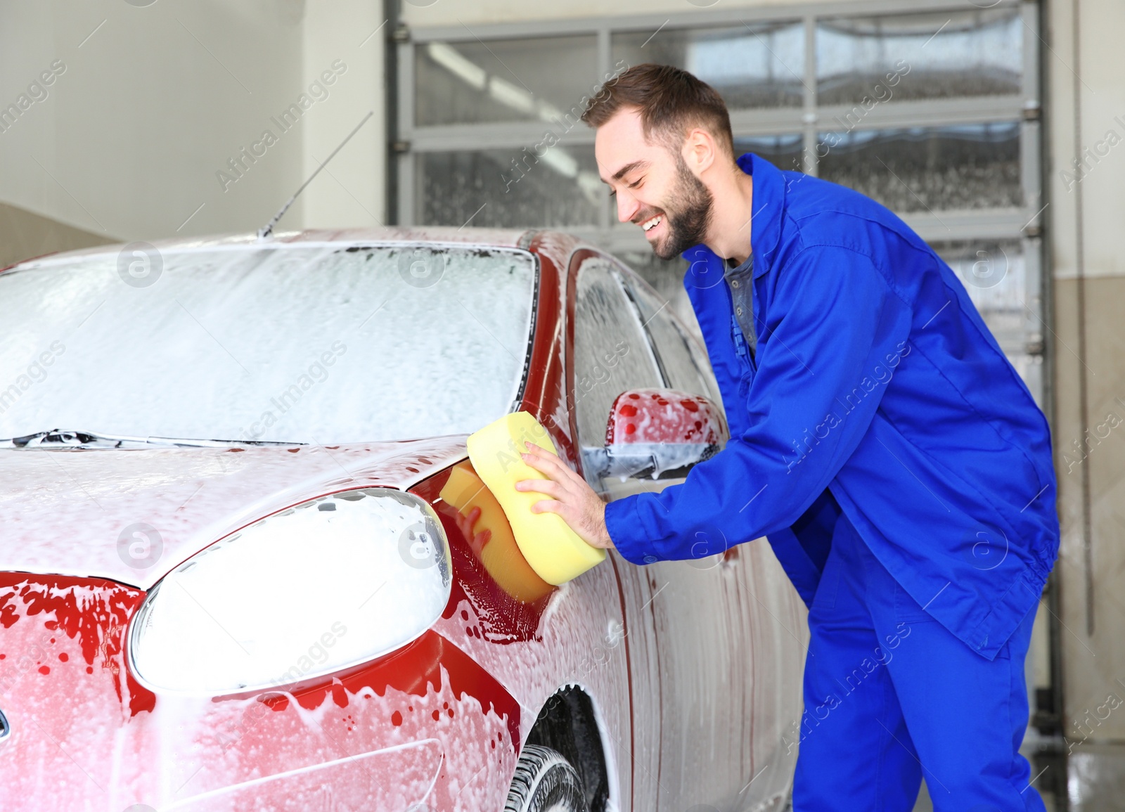 Photo of Worker cleaning automobile with sponge at professional car wash