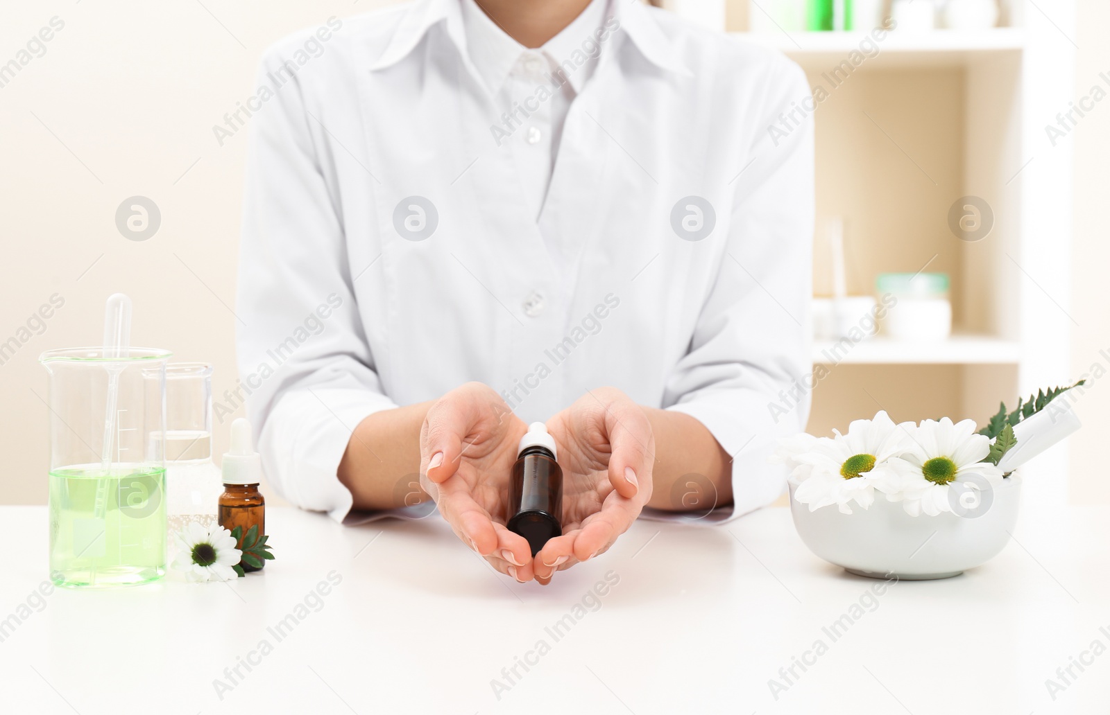 Photo of Female dermatologist holding bottle of skin care product at table, closeup