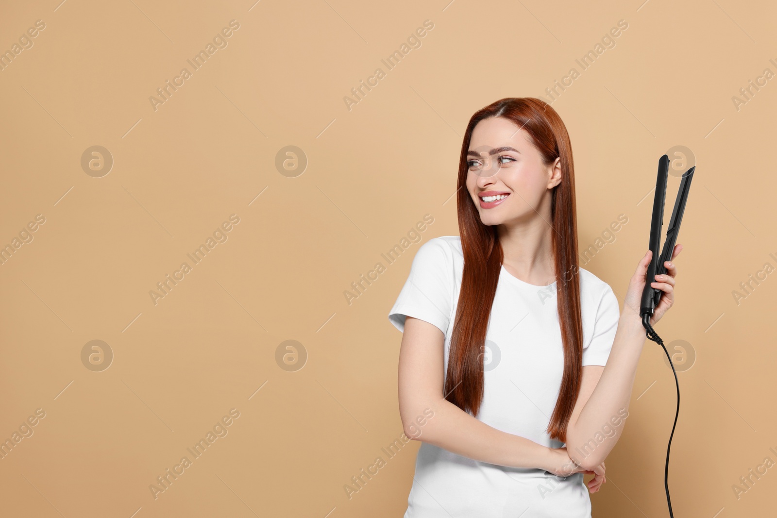 Photo of Beautiful woman with hair iron on beige background, space for text