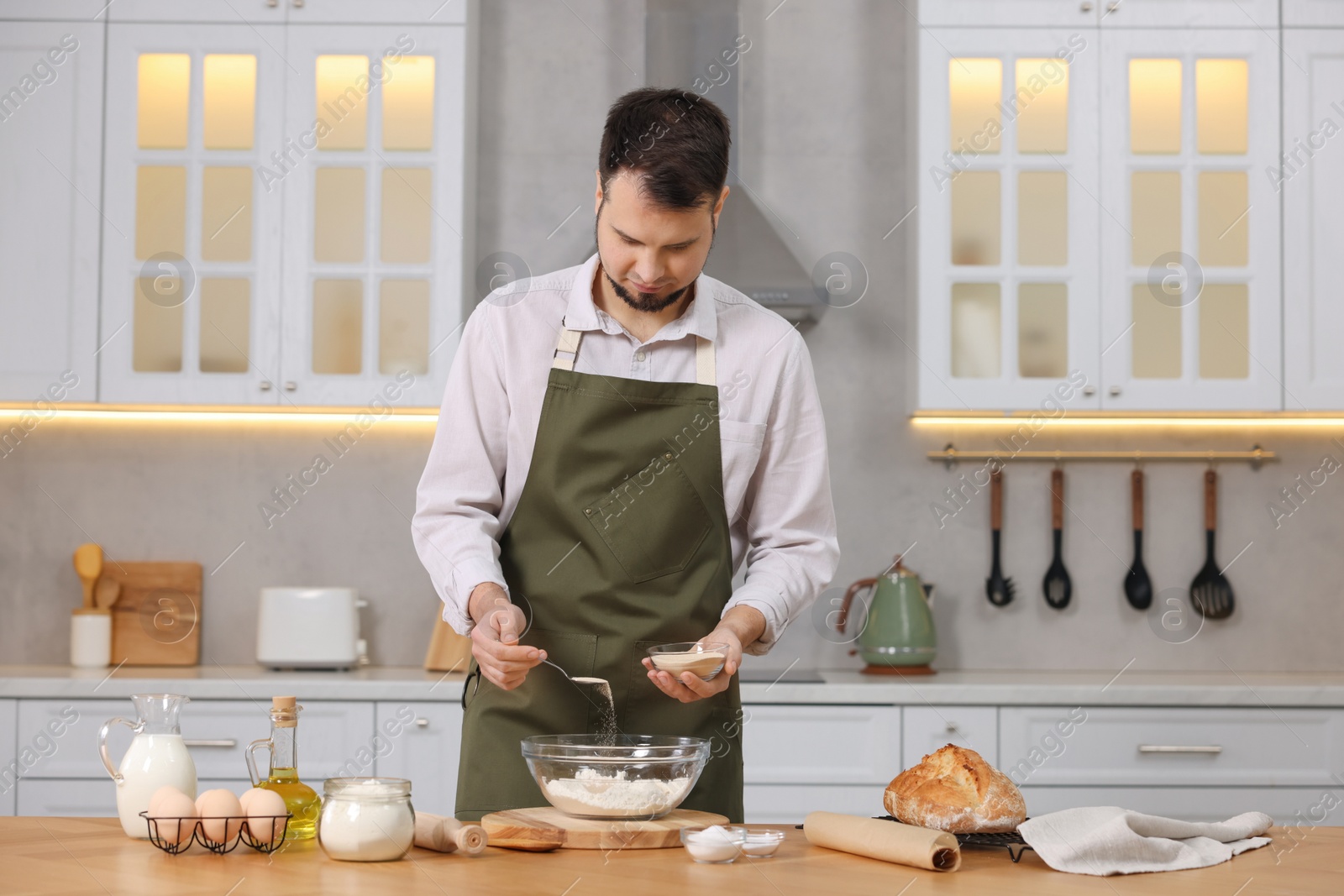 Photo of Making bread. Man putting dry yeast into bowl with flour at wooden table in kitchen