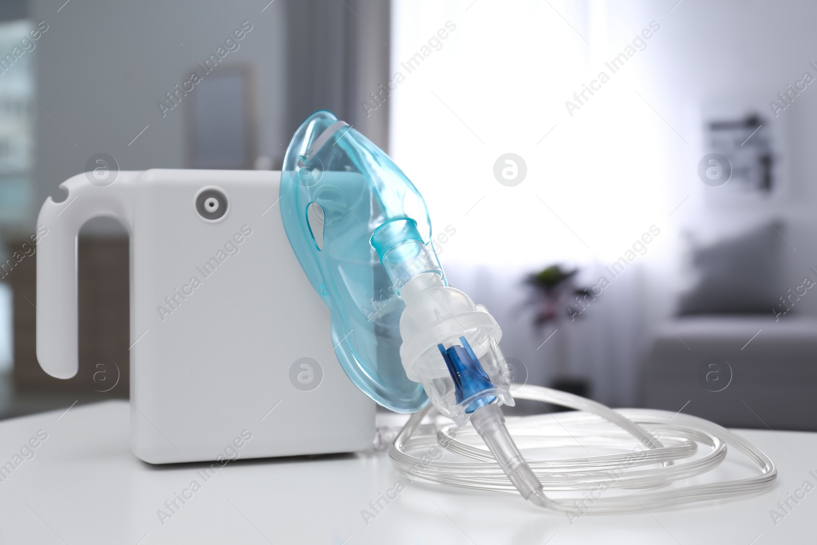 Photo of Modern nebulizer with face mask on white table indoors. Inhalation equipment
