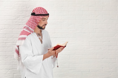 Photo of Muslim man reading Koran near brick wall. Space for text