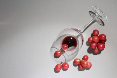 Overturned glass of wine and grapes on white background, flat lay. Space for text