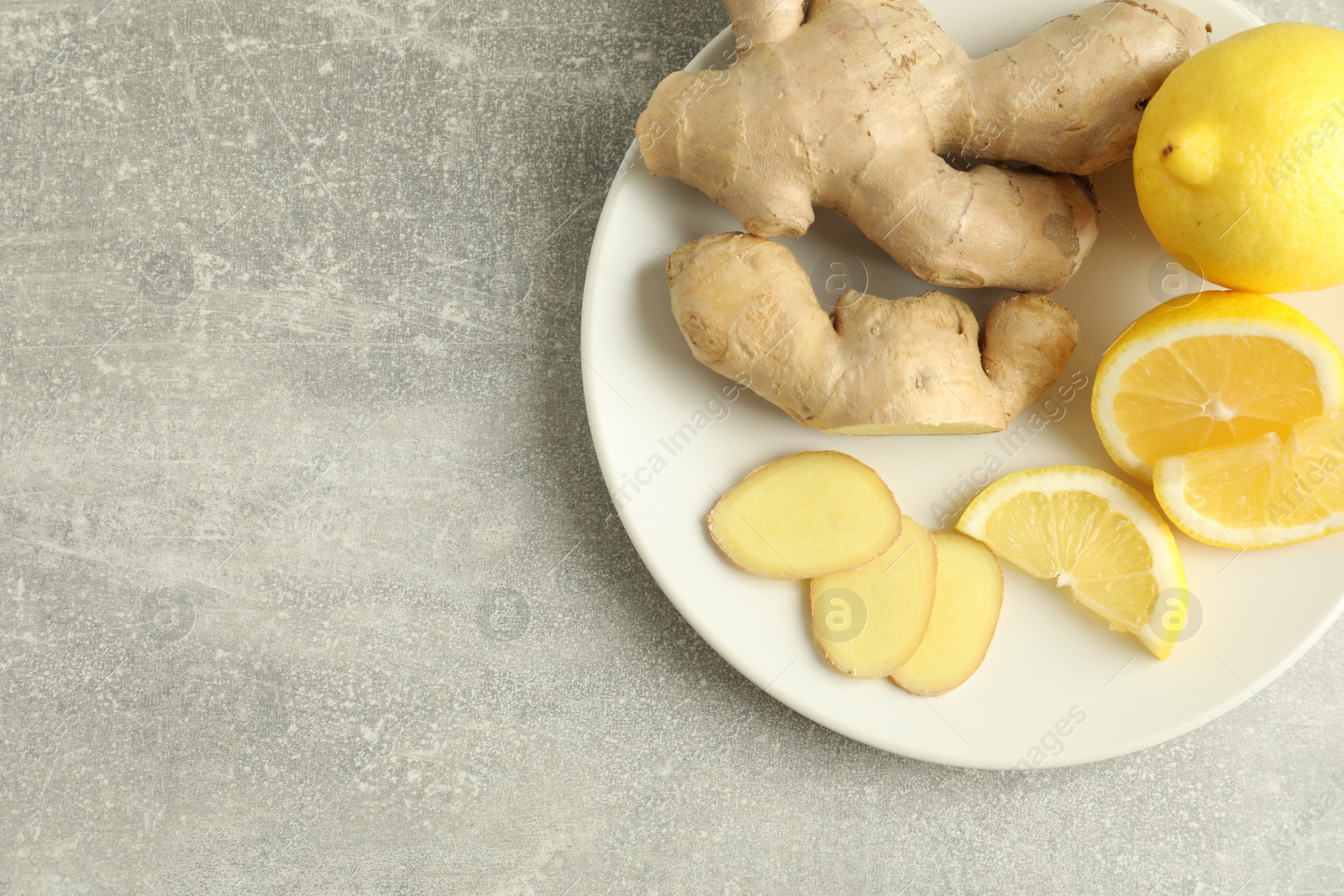 Photo of Fresh lemons and ginger on grey table, top view. Space for text