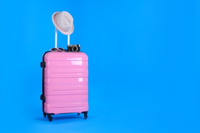 Photo of Travel suitcase with hat, camera and sunglasses on light blue background, space for text. Summer vacation