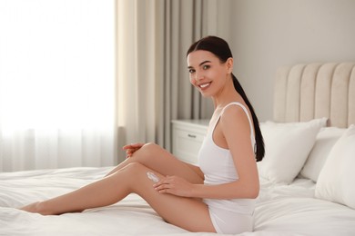Photo of Young woman applying body cream onto her leg at home, space for text