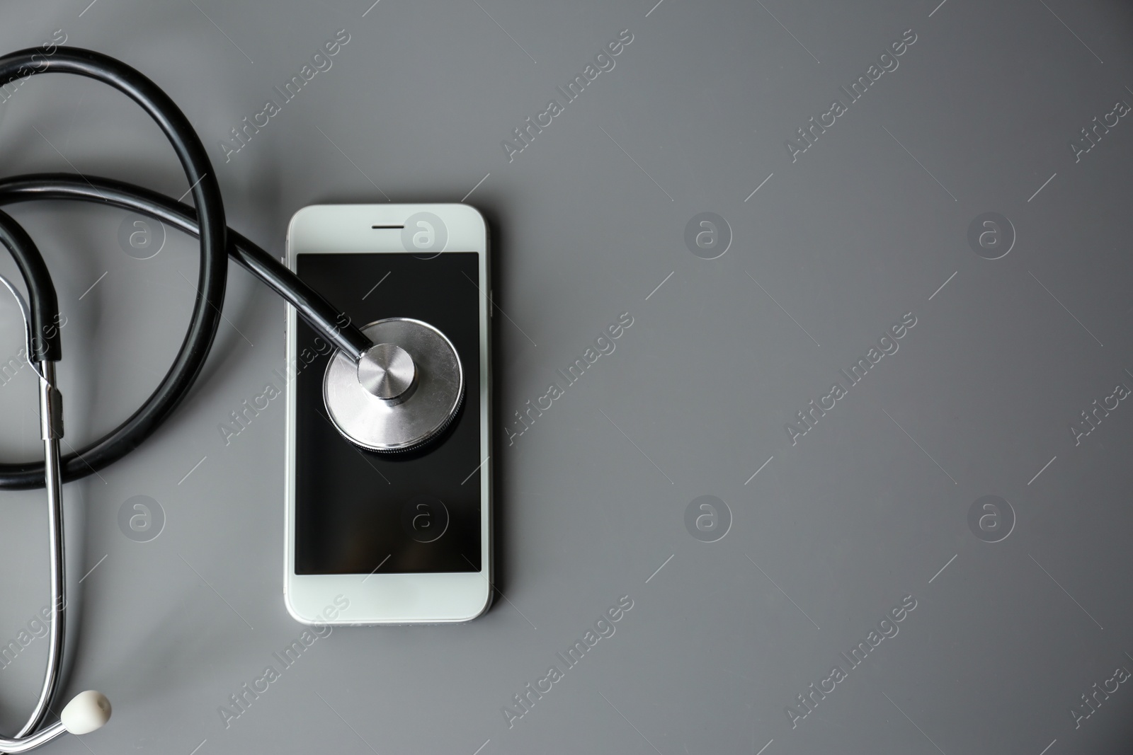 Photo of Smartphone and stethoscope on grey table, top view with space for text. Repairing service