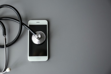 Photo of Smartphone and stethoscope on grey table, top view with space for text. Repairing service