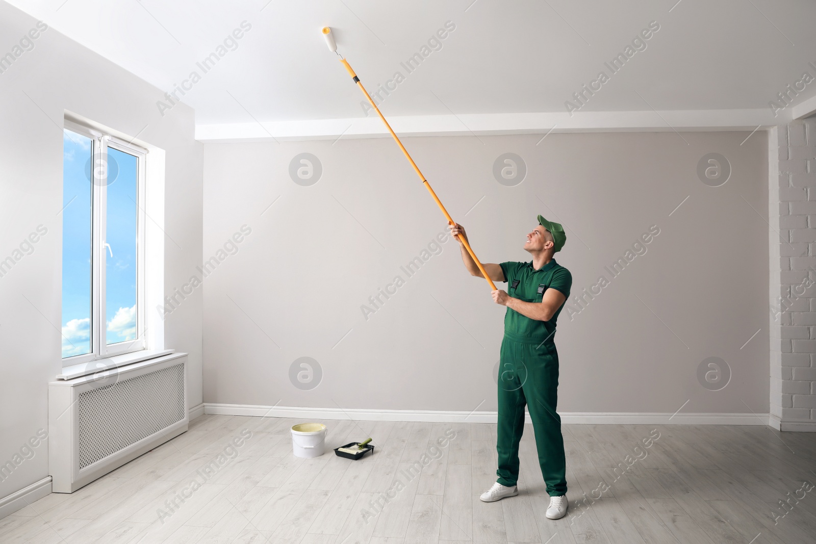 Photo of Man painting ceiling with roller in room