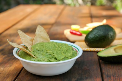 Photo of Delicious guacamole made of avocados and nachos on wooden table outdoors, space for text