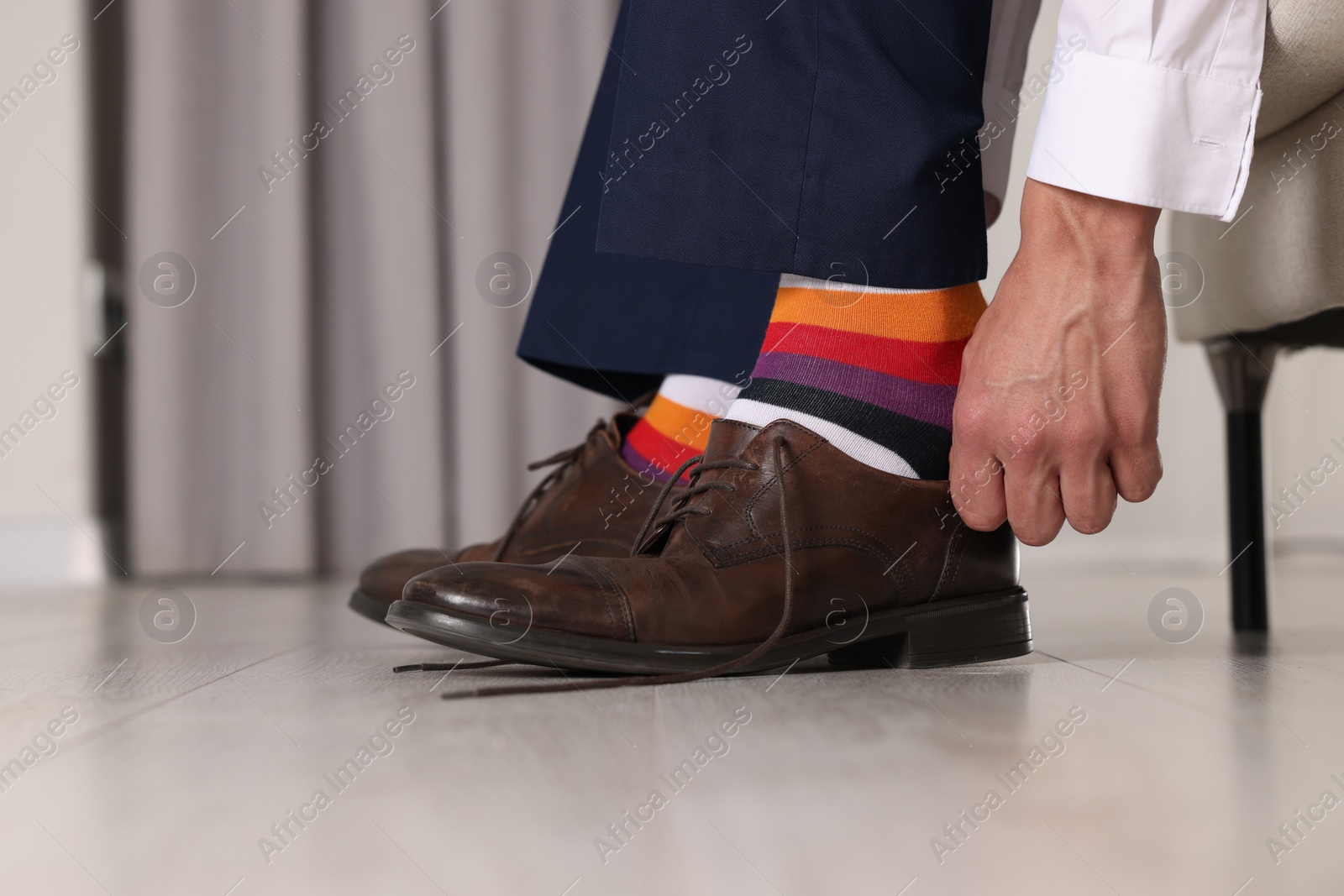 Photo of Man with colorful socks putting on stylish shoes indoors, closeup