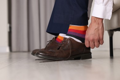 Man with colorful socks putting on stylish shoes indoors, closeup