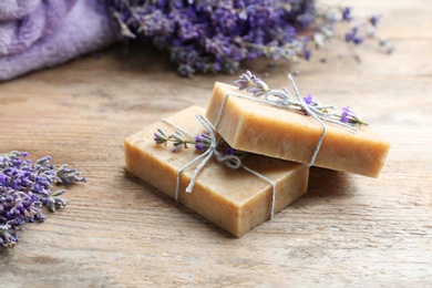 Photo of Handmade soap bars with lavender flowers on brown wooden table, closeup