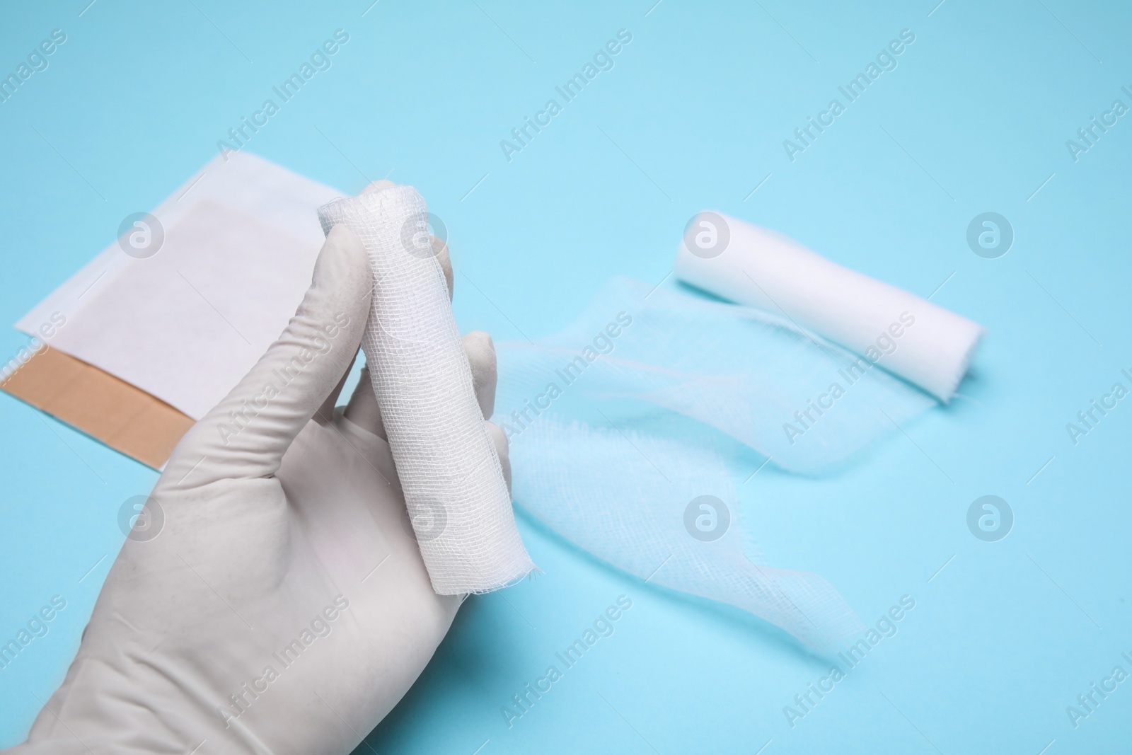 Photo of Doctor holding white bandage rolls on light blue background, closeup