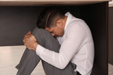 Photo of Scared man hiding under office desk during earthquake