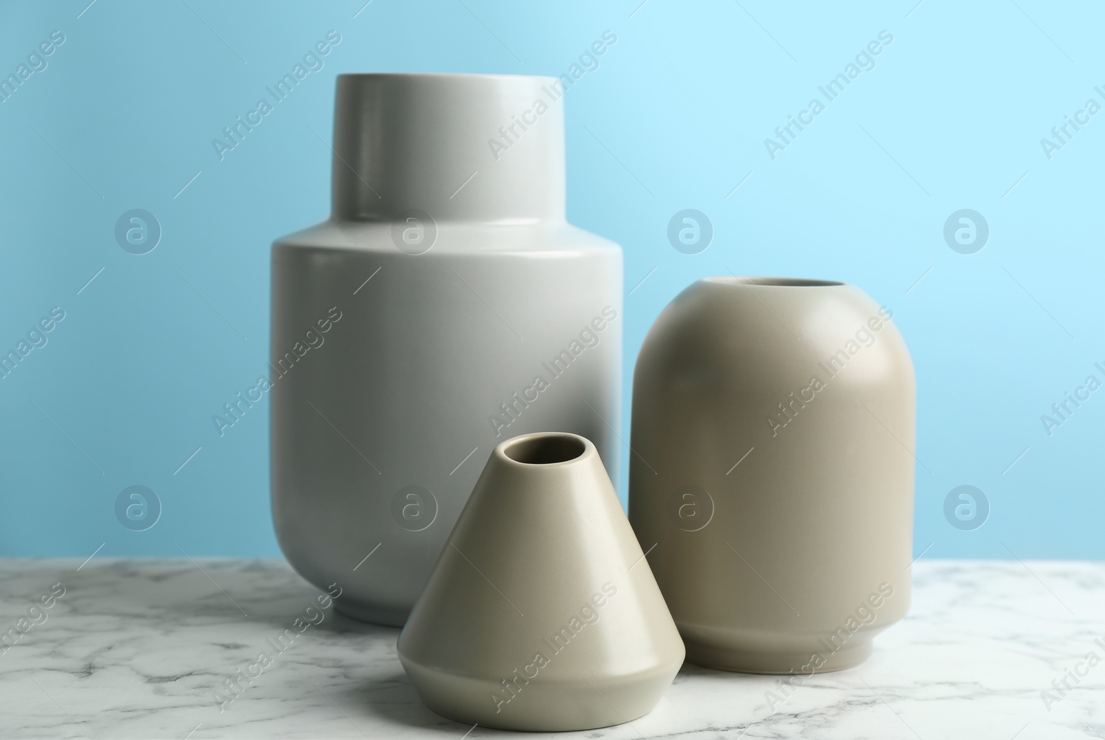 Photo of Stylish empty ceramic vases on white marble table against light blue background