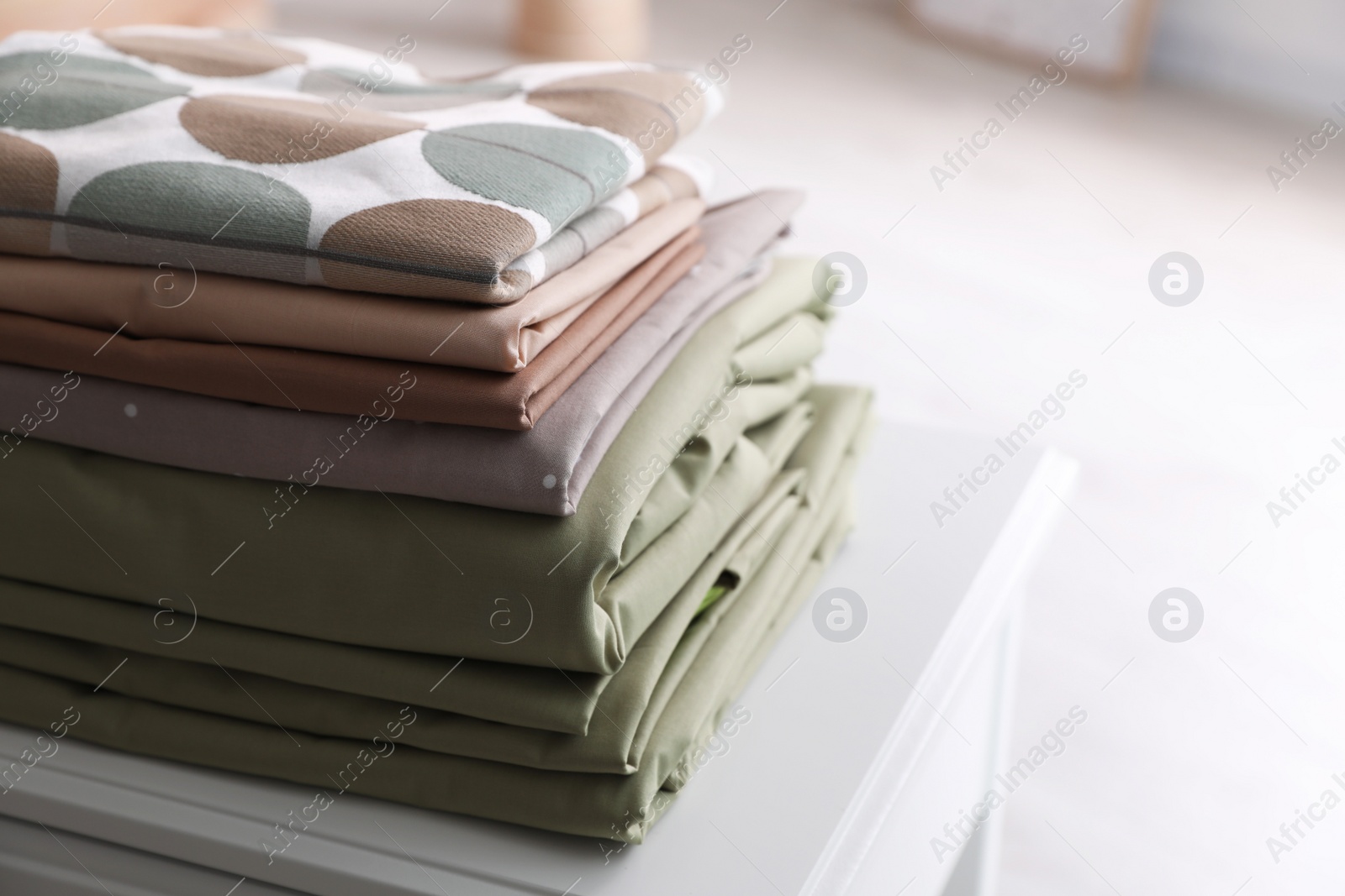 Photo of New clean folded bed linens on table indoors. Space for text