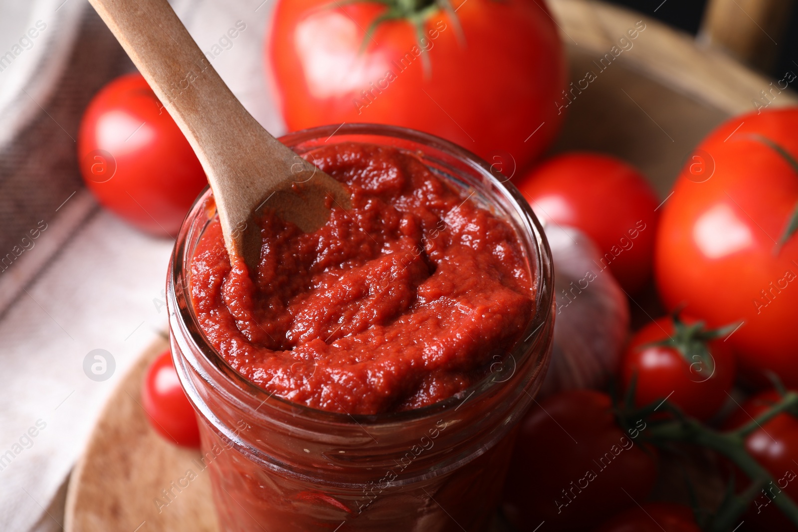 Photo of Taking tasty tomato paste with spoon from jar on table, closeup