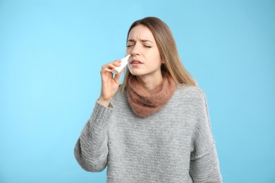 Photo of Sick young woman using nasal spray on light blue background