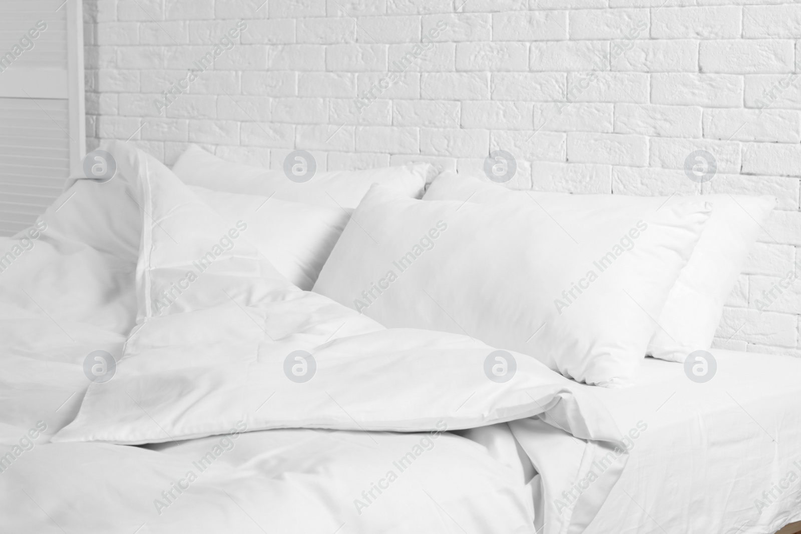 Photo of Large comfortable bed with pillows and blanket near white brick wall indoors. Stylish interior