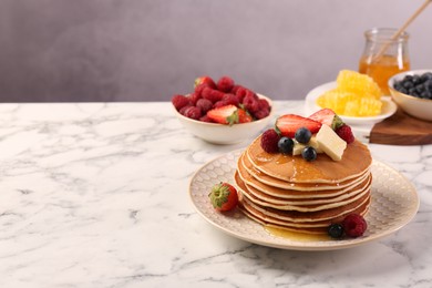 Photo of Delicious pancakes with fresh berries, butter and honey on white marble table, space for text
