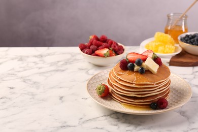 Delicious pancakes with fresh berries, butter and honey on white marble table, space for text