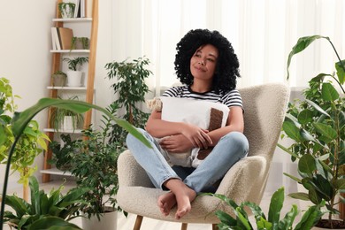 Woman relaxing in armchair surrounded by beautiful houseplants at home