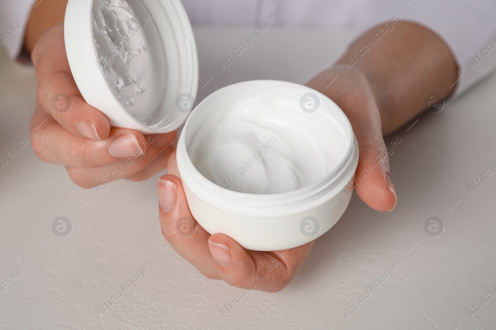 Photo of Dermatologist holding jar of cream at white table, closeup. Developing cosmetic product