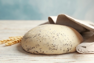 Photo of Raw dough with poppy seeds under towel on wooden table