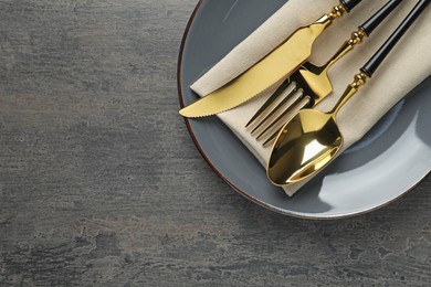 Photo of Elegant setting with golden cutlery on dark grey table, top view. Space for text