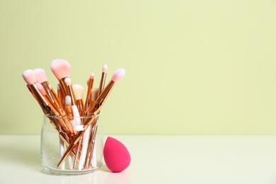 Jar with makeup brushes and sponge on table. Space for text