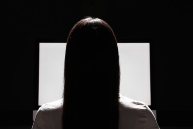 Woman using computer in dark room, back view. Internet addiction