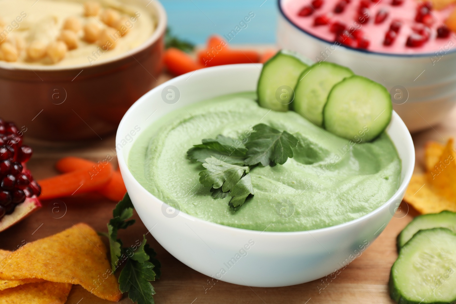 Photo of Bowl of delicious green hummus with parsley and cucumber on wooden table