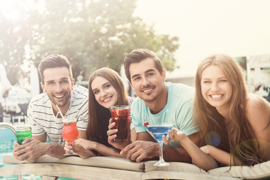 Image of Happy young friends with fresh summer cocktails relaxing near swimming pool