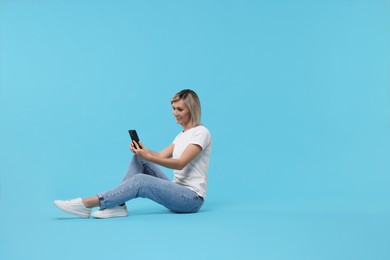 Photo of Happy woman with phone on light blue background, space for text