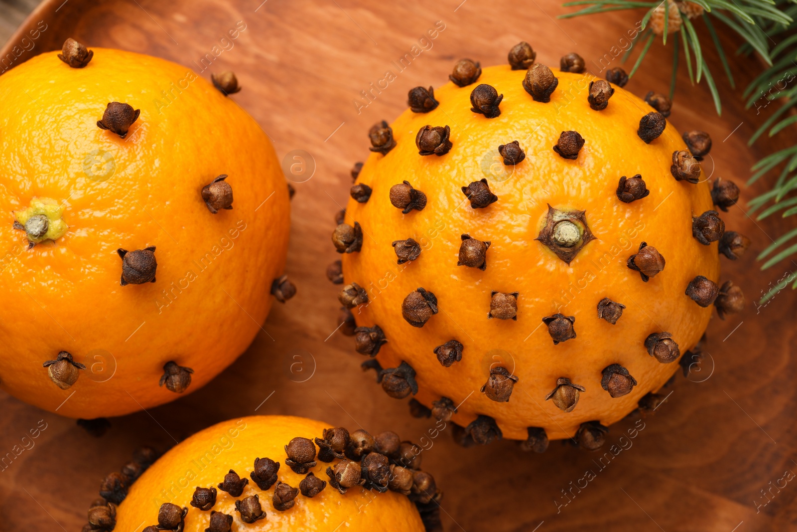Photo of Pomander balls made of tangerines with cloves on wooden plate, top view