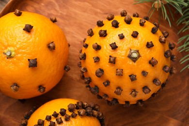 Pomander balls made of tangerines with cloves on wooden plate, top view