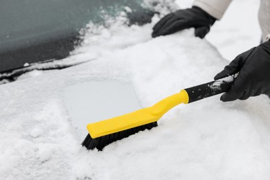 Photo of Man cleaning snow from car hood outdoors, closeup